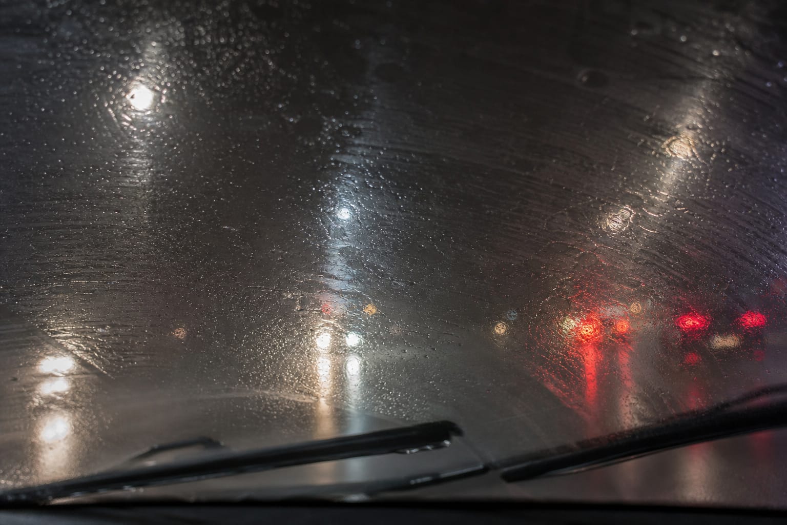 Gros plan sur un pare-brise de voiture sous la pluie avec des traces et un voile laissés par l'essuie-glace
