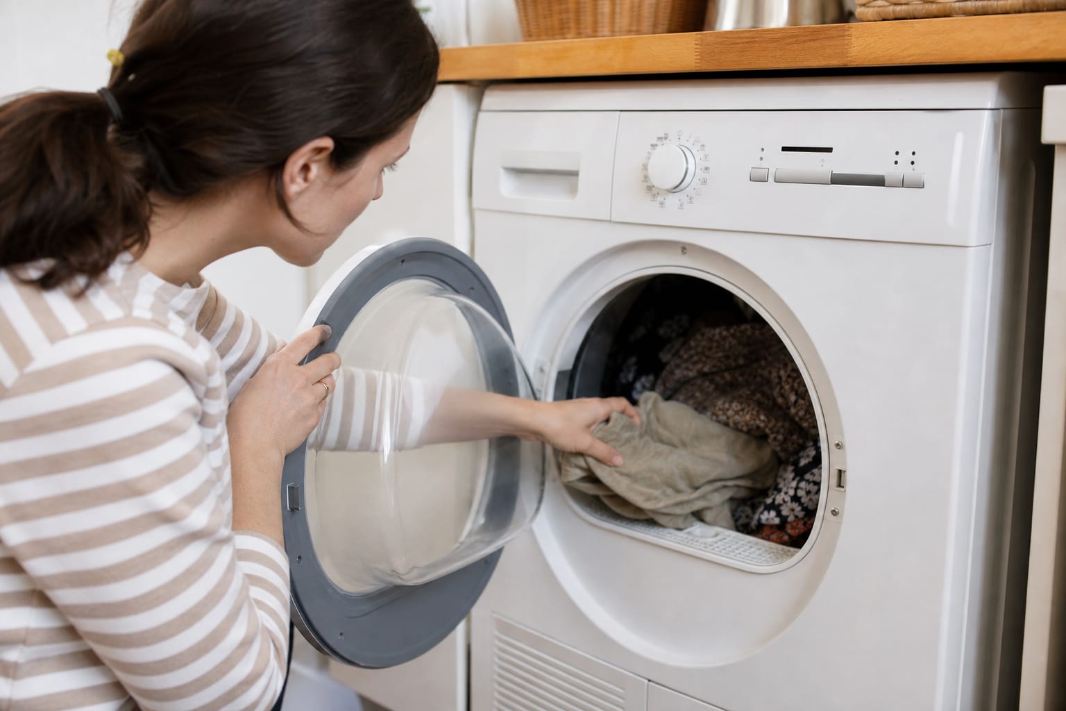 Personne ouvrant la porte d'un sèche-linge dans une buanderie pour vérifier du linge encore humide