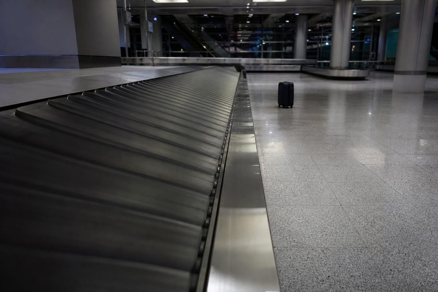 Tapis à bagages vide dans un aéroport avec une seule valise abandonnée au loin, hall d'arrivée désert
