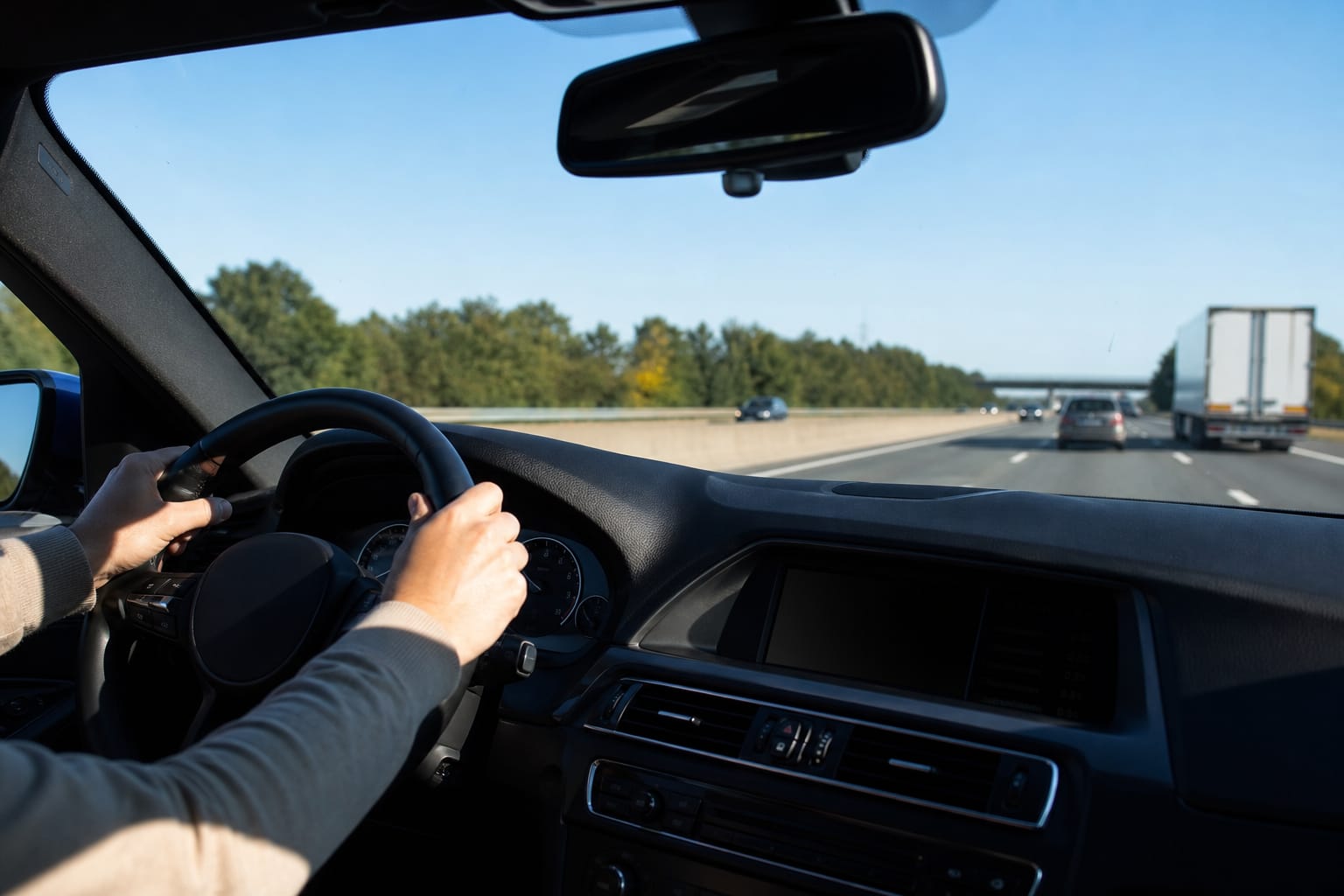 Vue depuis l'intérieur d'une voiture roulant sur une autoroute, mains sur le volant, ligne blanche légèrement décentrée vers la droite