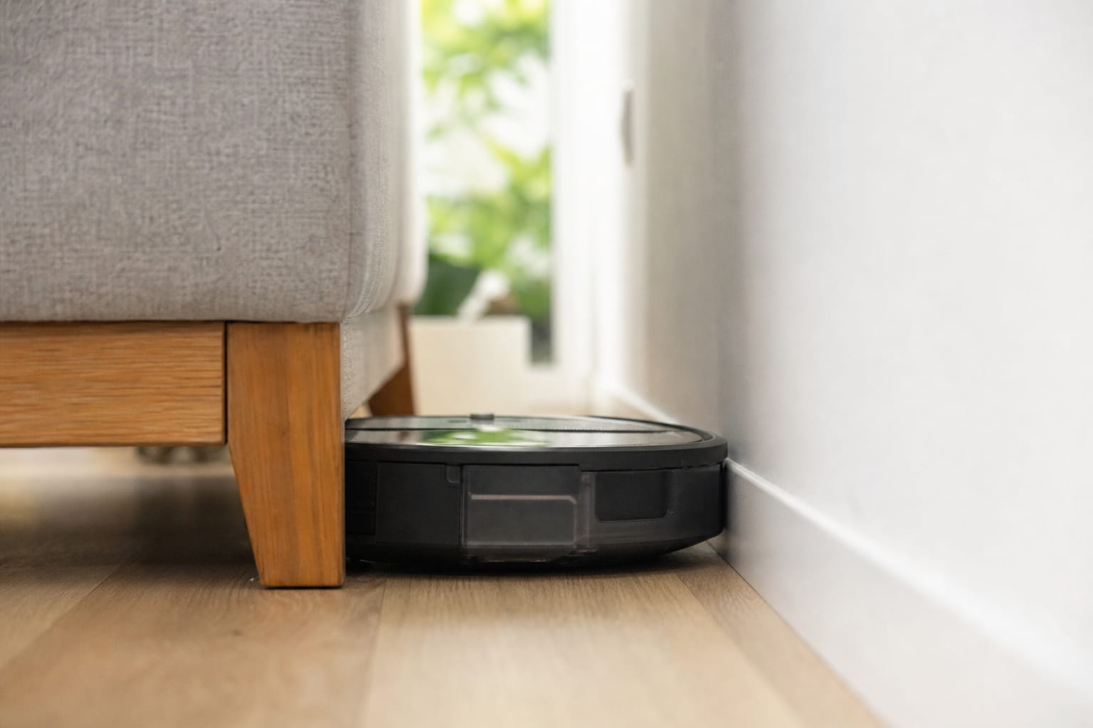 Aspirateur robot coincé contre le pied d'un canapé dans un salon, vue au ras du sol