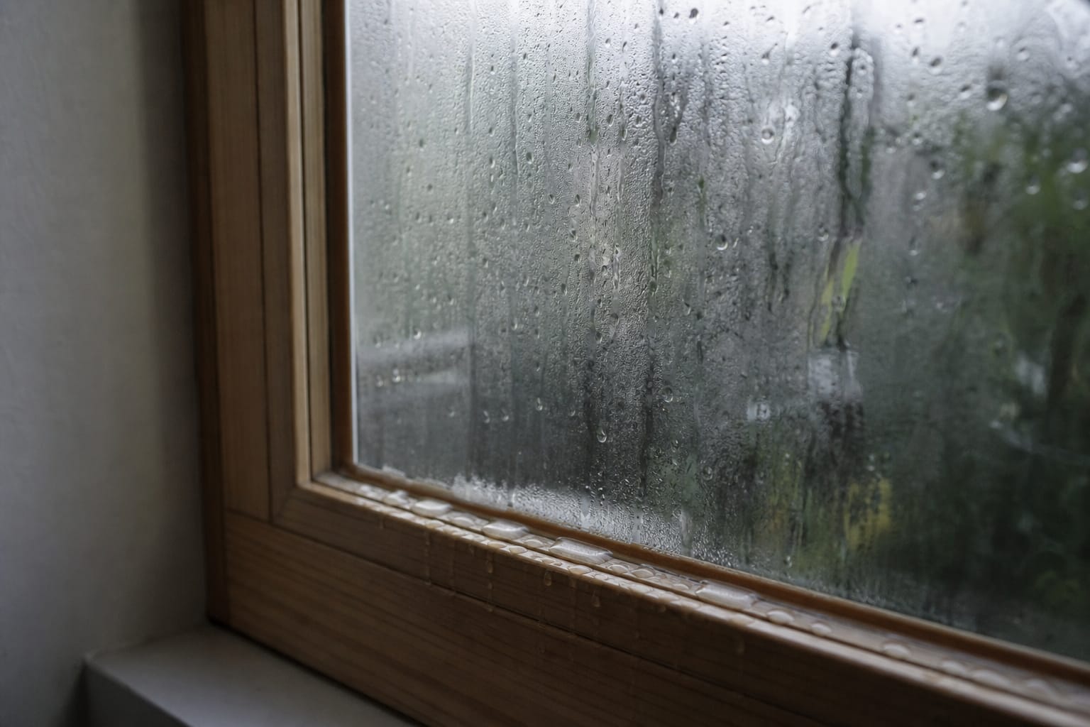 Vitre de fenêtre couverte de condensation au petit matin, gouttes d'eau ruisselant vers le bas du cadre en bois