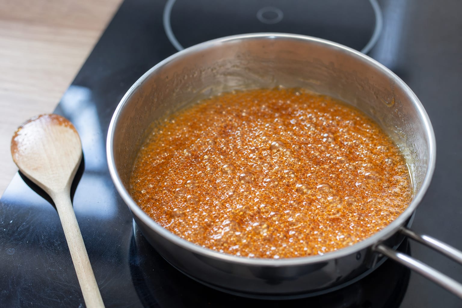 Casserole de caramel doré en train de cuire sur une plaque de cuisson, cuillère en bois posée à côté
