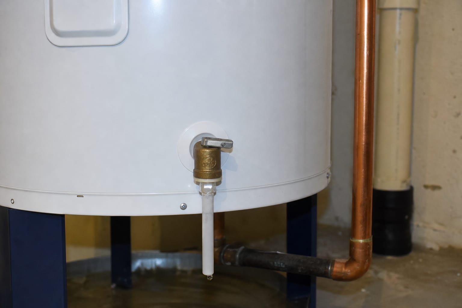Chauffe-eau électrique blanc dans une cave, tuyau de la soupape de sécurité visible avec une goutte d'eau