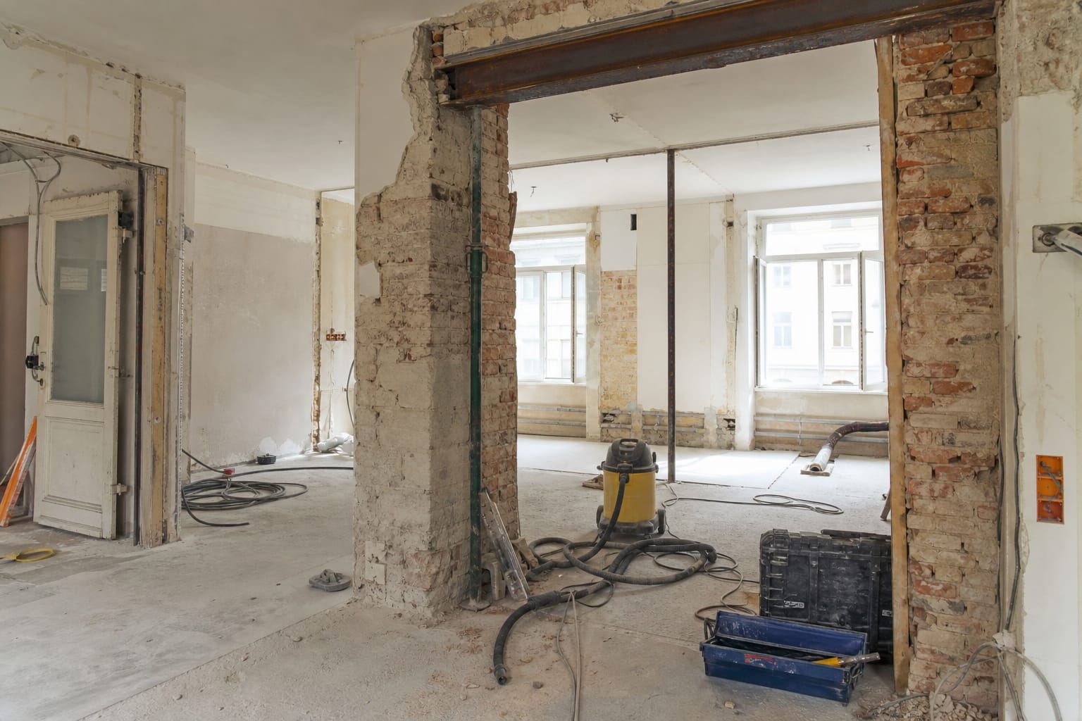 Intérieur d'un appartement en travaux, mur partiellement ouvert laissant apparaître une structure en briques, outils de démolition posés au sol