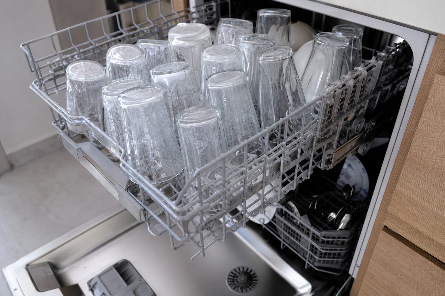 Verres empilés dans le panier supérieur d'un lave-vaisselle ouvert, surface légèrement voilée d'un film blanc calcaire