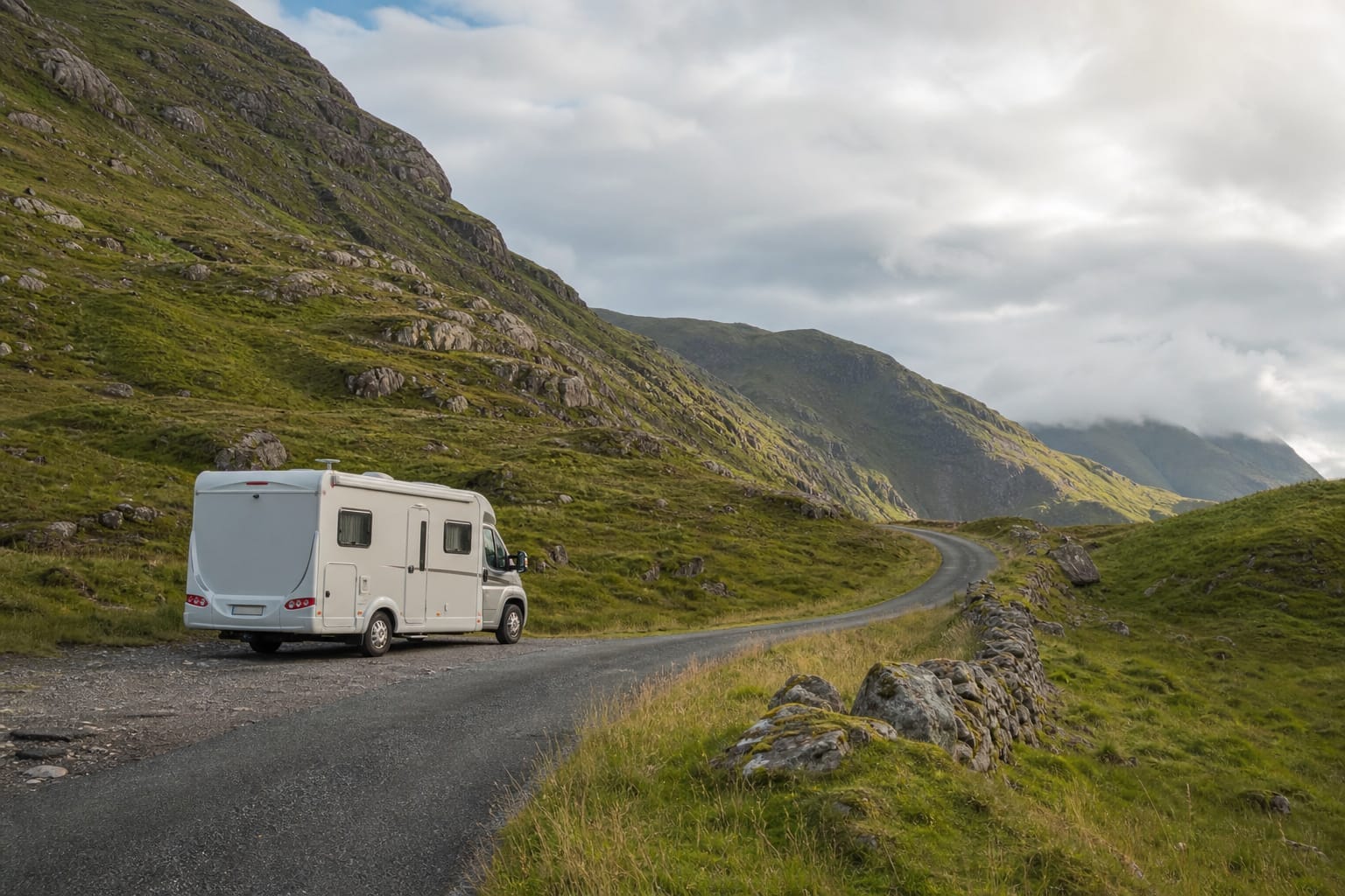 Camping-car garé sur une route sinueuse des Highlands écossais, entre collines vertes et loch au premier plan