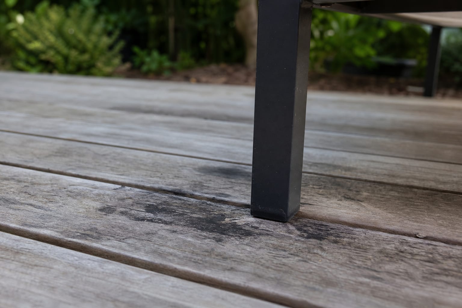 Lames de terrasse en bois grisées avec des taches noires par endroits, vue rapprochée au niveau du sol