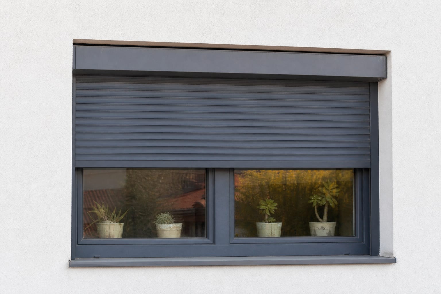 Volet roulant électrique arrêté à mi-hauteur sur une fenêtre de maison, moitié ouvert moitié fermé